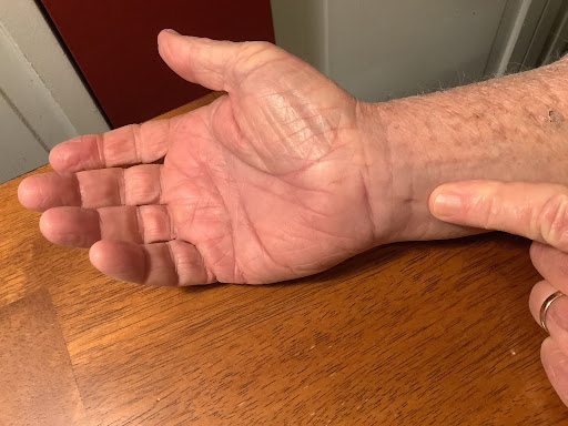 Close-up of a relaxed hand on a textured wooden table, showcasing age and care.