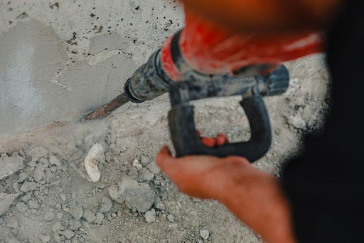 Individual using a red jackhammer for construction work on concrete at a busy site.