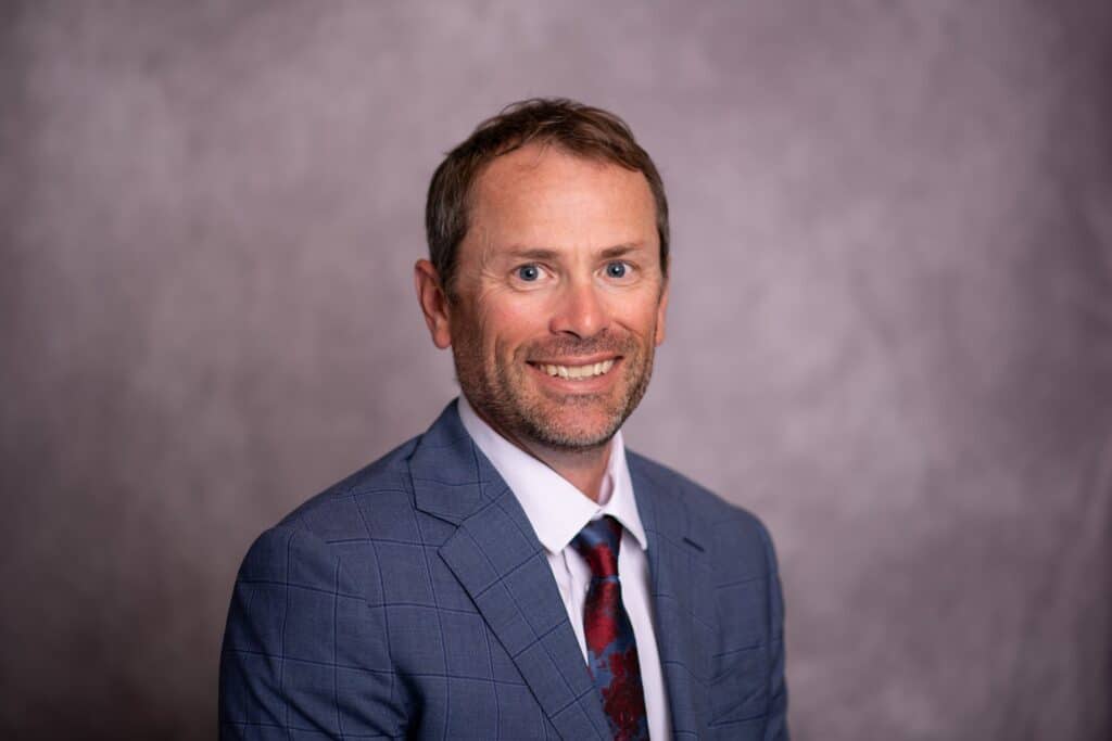 Dr. Craig Chappell in a blue suit with floral tie, exuding professionalism and approachability.