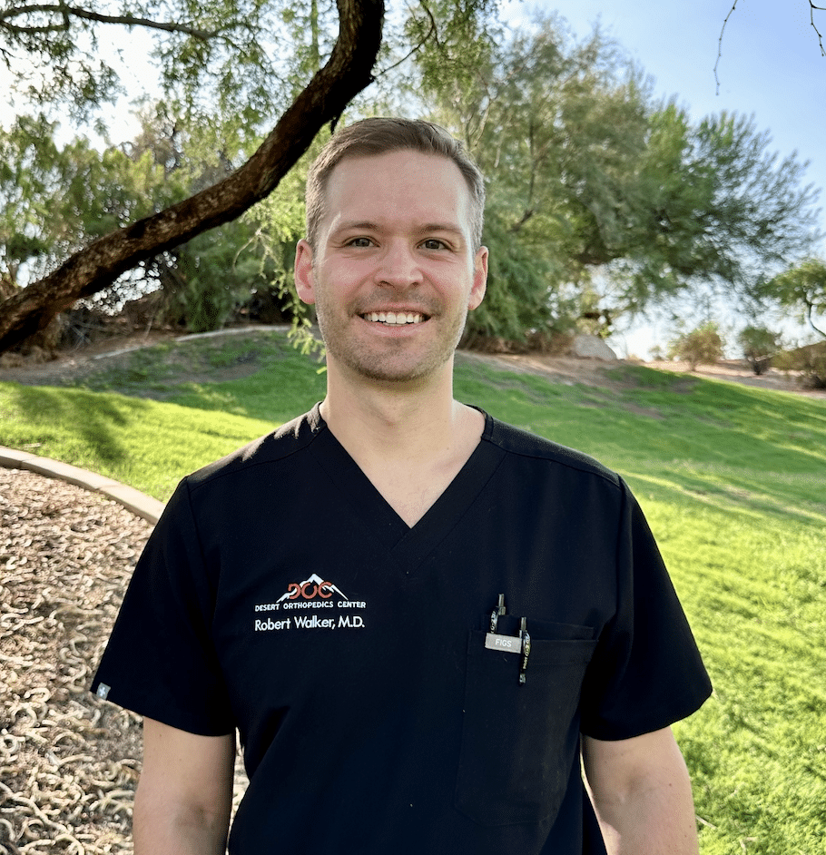 Smiling doctor in black scrubs outdoors at Desert Orthopedics Center, showcasing professionalism and approachability.
