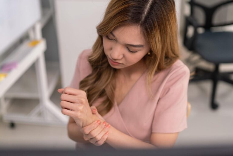 Woman examining her wrist at a tidy desk, reflecting on self-care and well-being.