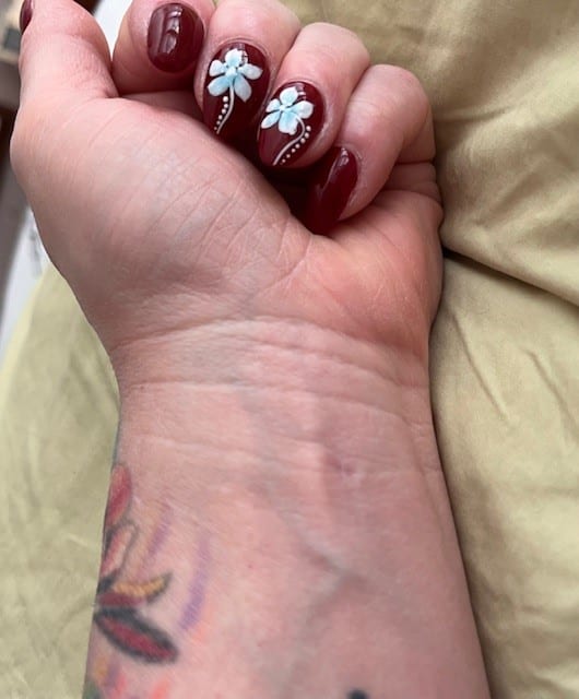 Artistic burgundy manicure with floral designs, showcasing a tattoo on a relaxed hand.