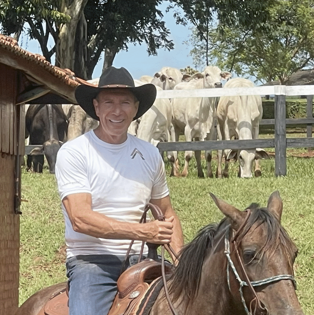 Man riding a brown horse in a serene rural landscape with cattle and blue skies.