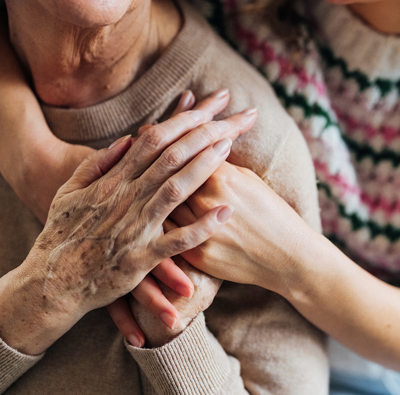 younger woman lovingly places hands around older woman on shoulder.